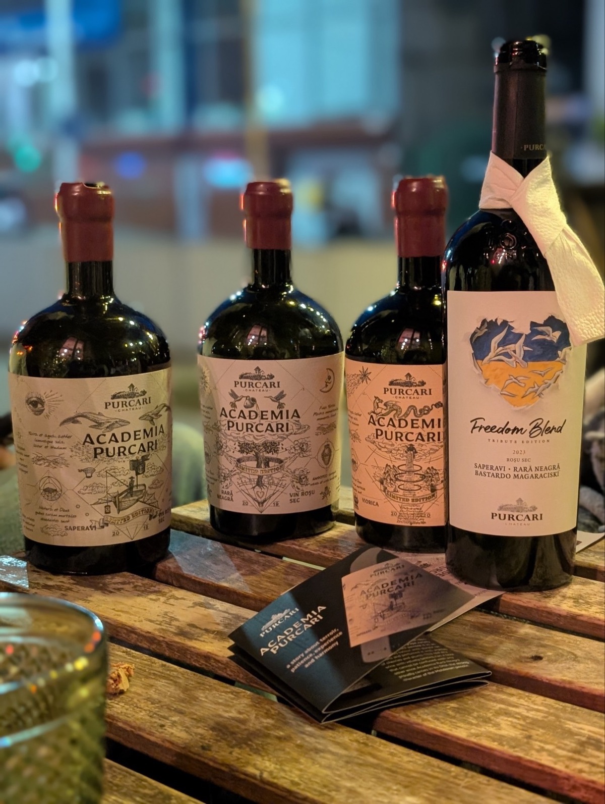 Cele patru sticle pe masă — trei Academia Purcari și un Freedom Blend, lângă broșura seriei