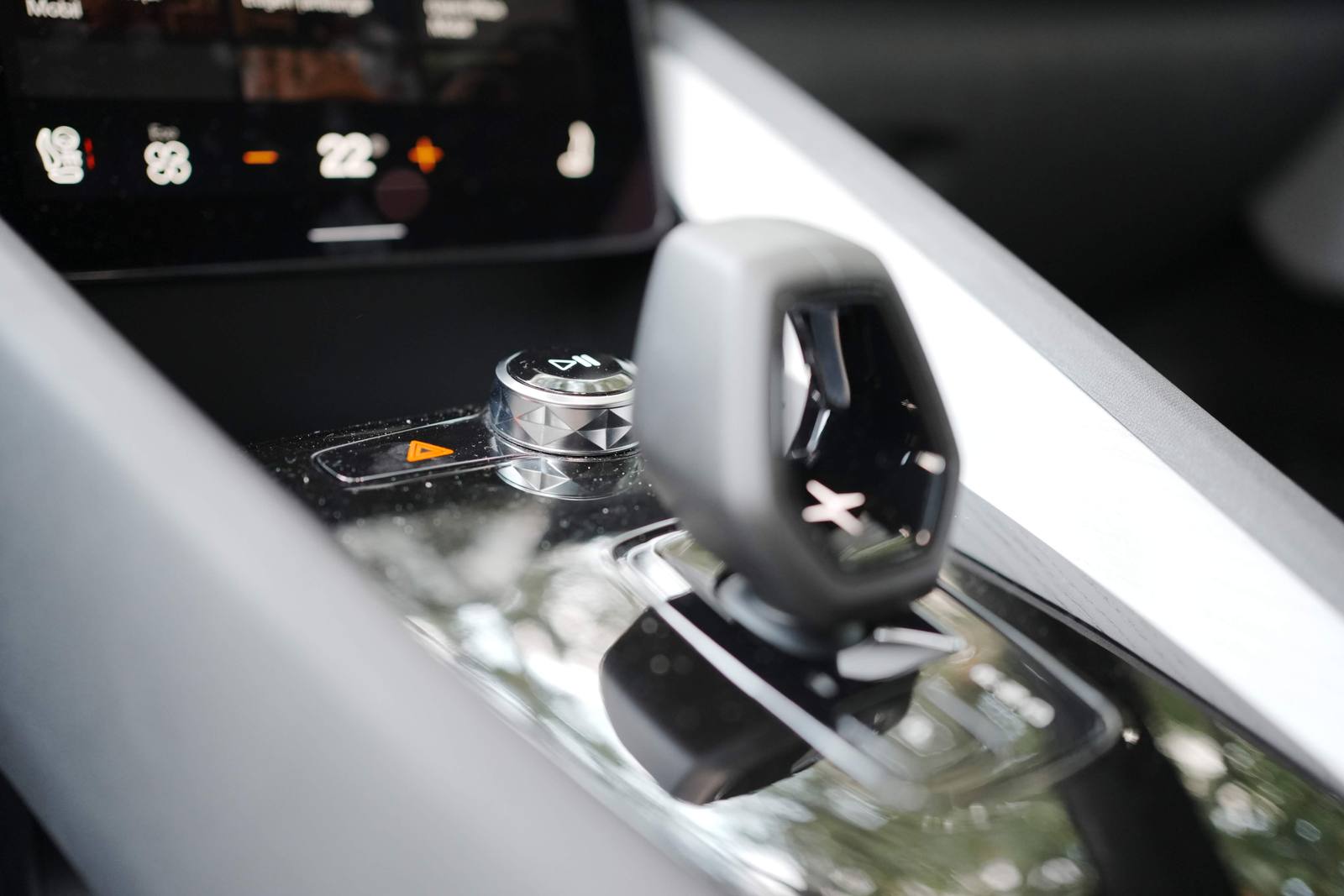 The volume knob with the pause symbol and the hazard button on the console; above, the climate bar on the screen