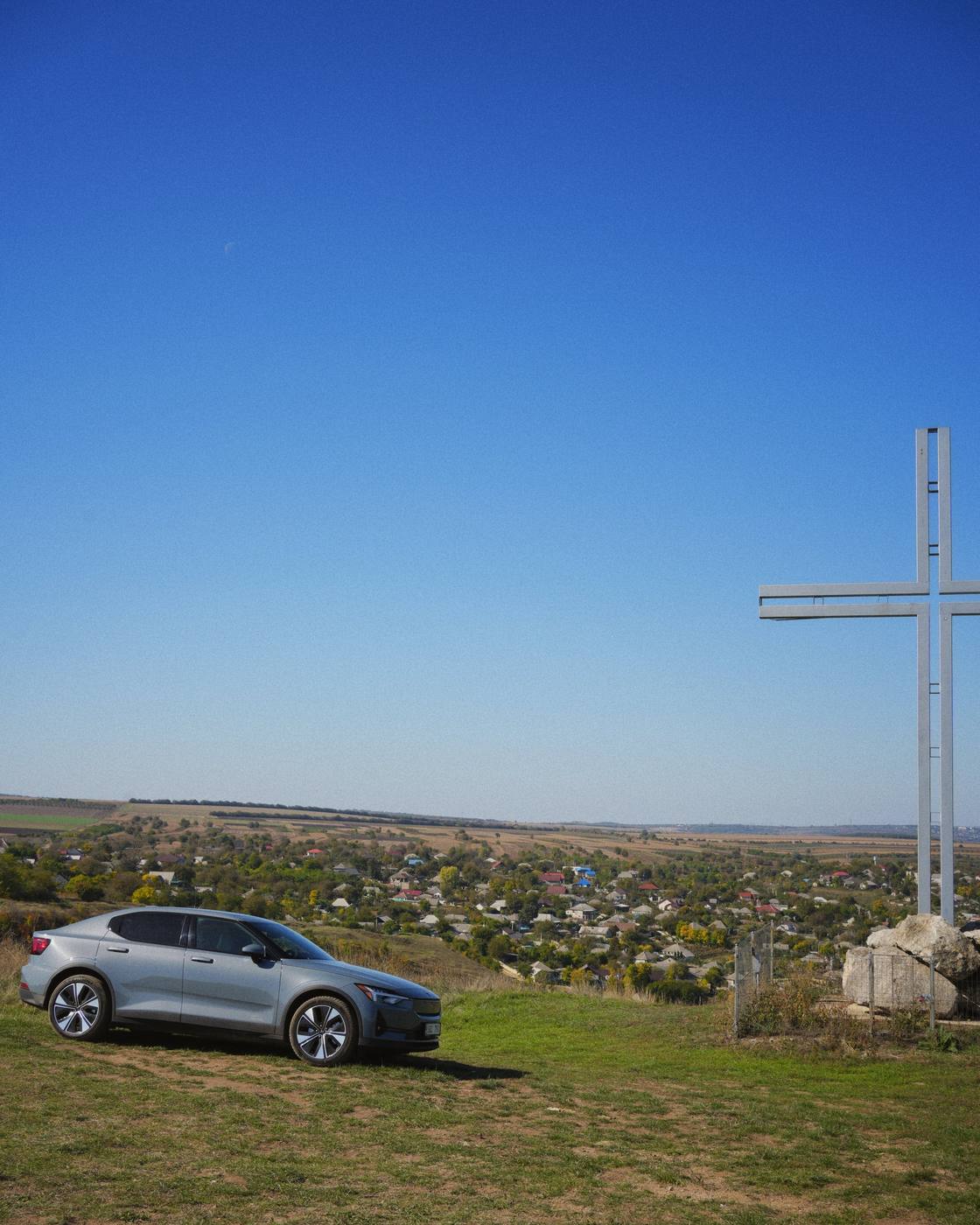 The car next to the big cross at the viewpoint, with the village in the valley