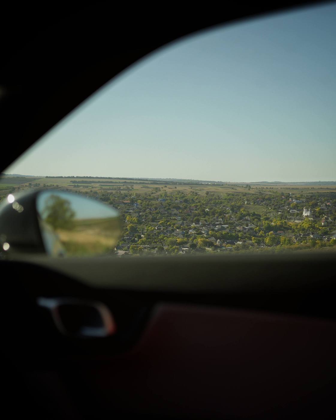 The driver's window and mirror; outside, the village in the distance