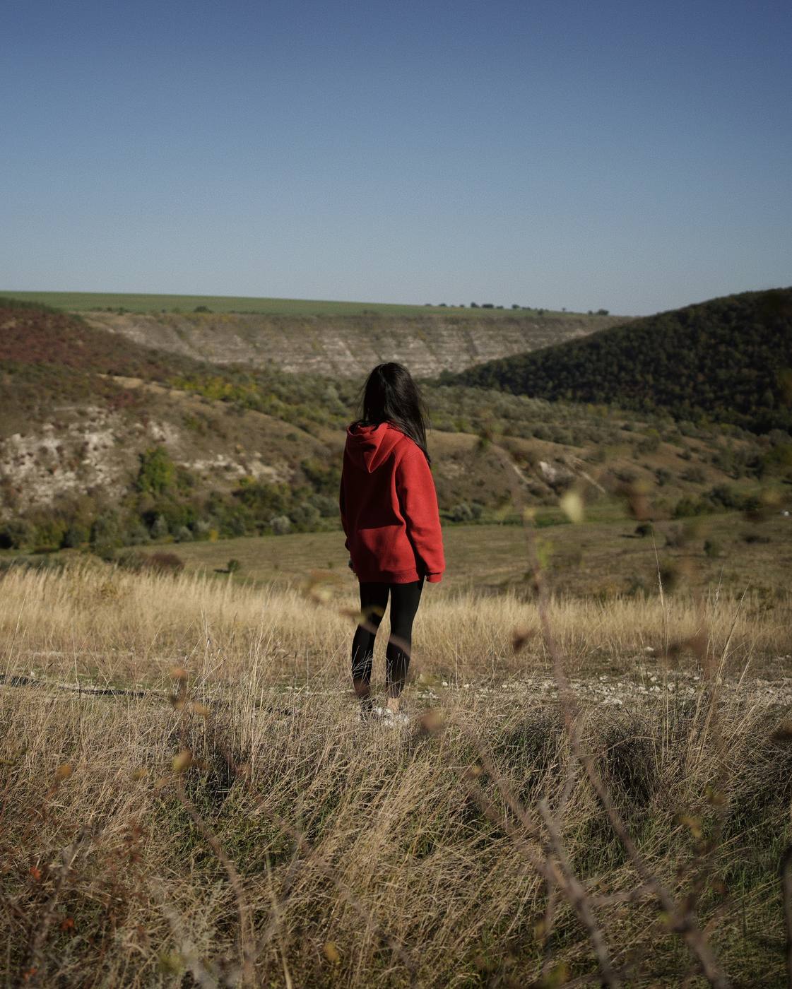 My better half, in a red jacket, in the tall grass, facing the hills and the rock banks